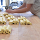 On a wooden work surface, chocolatines lie stacked up while a bakery employee folds them and stacks them.